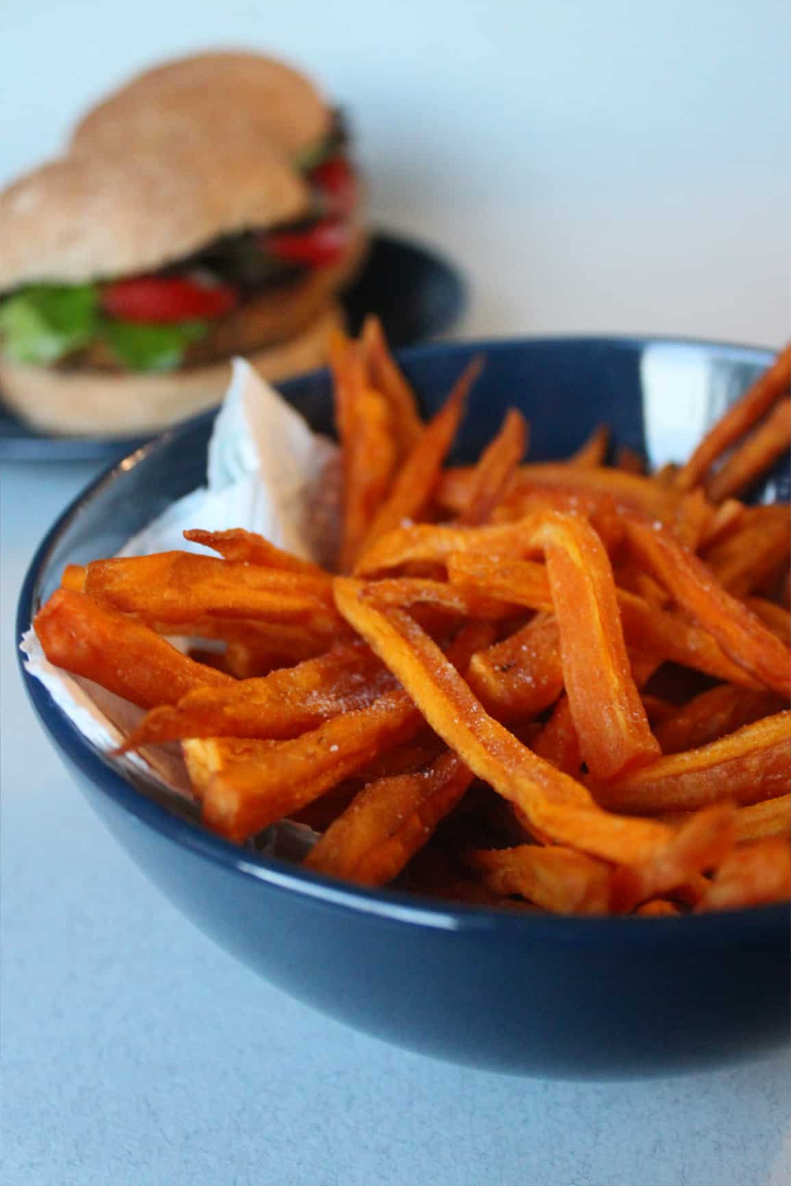 sweet potato fries in a bowl with burgers in background